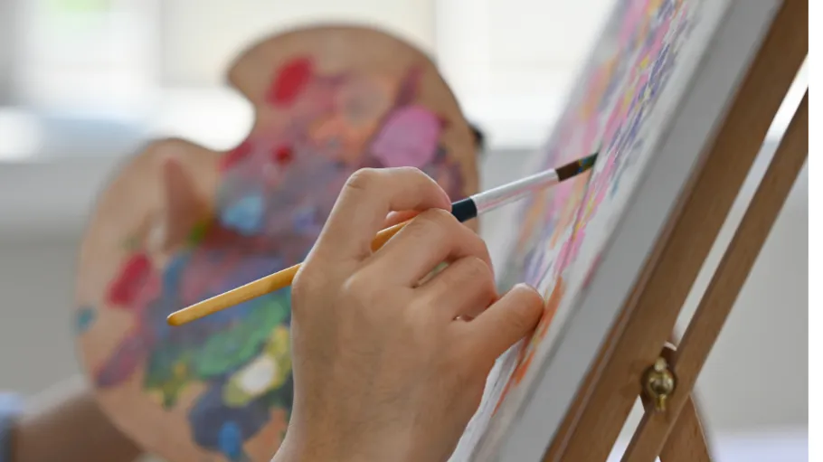 Person paint on canvas using palette indoors.