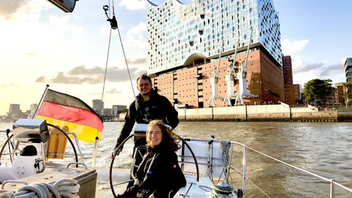 People sailing near modern building, German flag visible.