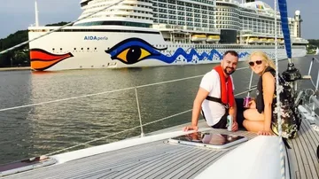 Two people on yacht near large cruise ship.
