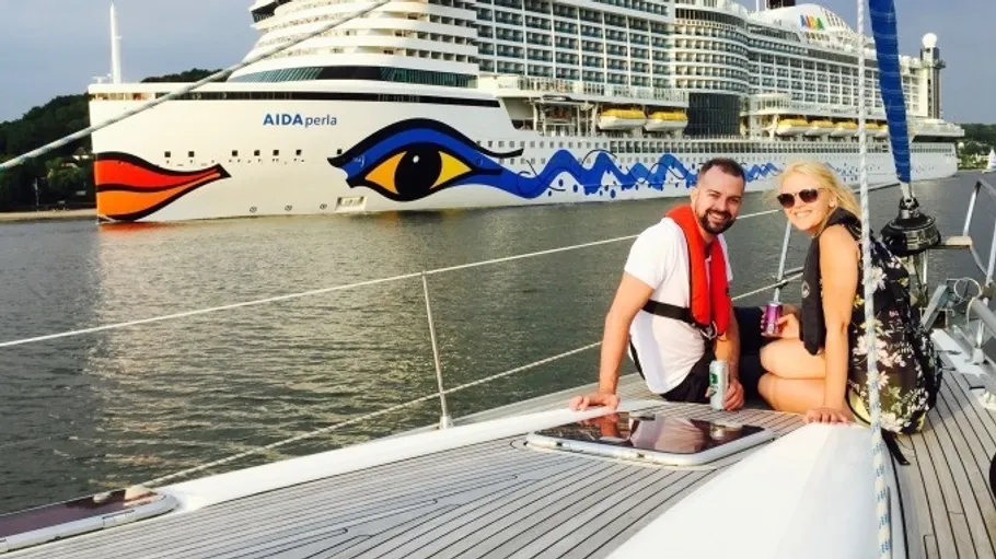 Two people on yacht near large cruise ship.
