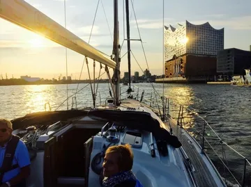 Sailboat on water near modern building at sunset.