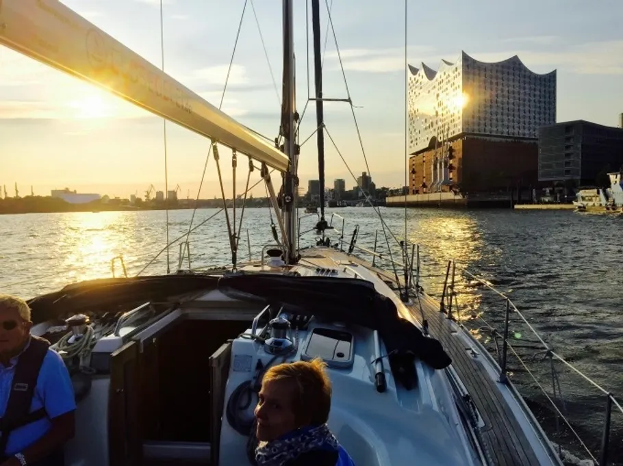 Segelboot auf Wasser nahe modernem Gebäude bei Sonnenuntergang.