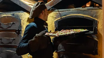 Baker places pizza in traditional oven.