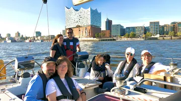 Gruppe auf Segelboot mit Stadtsilhouette im Hintergrund.