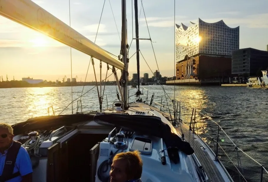 Segelboot auf Wasser nahe modernem Gebäude beim Sonnenuntergang.