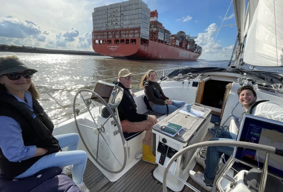 Segelboot mit Personen nahe großem Frachtschiff.