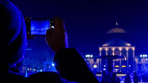Person photographing illuminated building at night.
