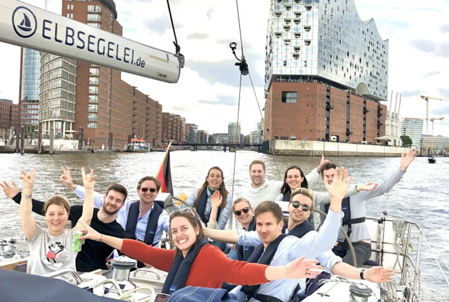 Group smiling on sailboat in city harbor.