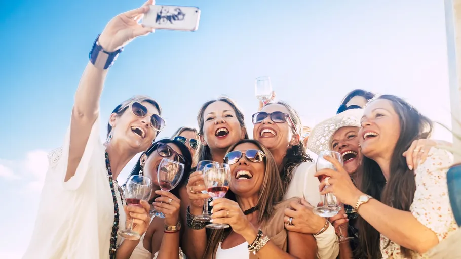 Gruppe Frauen macht Selfie mit Getränken draußen.