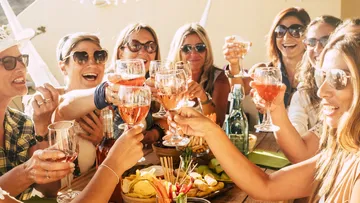 Gruppe von Frauen stößt draußen mit Getränken an.