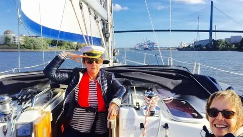 Person saluting on sailboat, bridge in background.