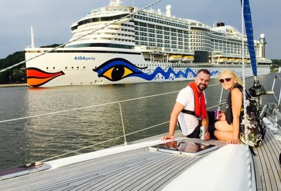 Couple sitting on sailboat near cruise ship.