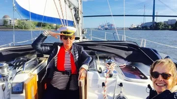 Zwei Personen auf Segelboot mit Brücke im Hintergrund.