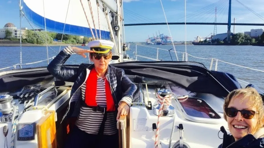 Zwei Personen auf Segelboot mit Brücke im Hintergrund.