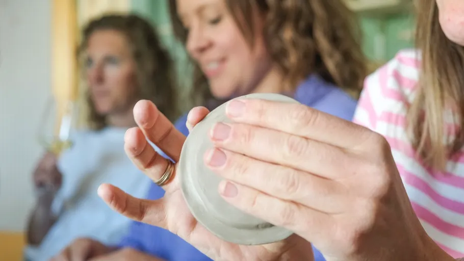 Person shaping clay with hands, others in background.