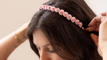 Woman adjusting pink flower headband, indoor setting.