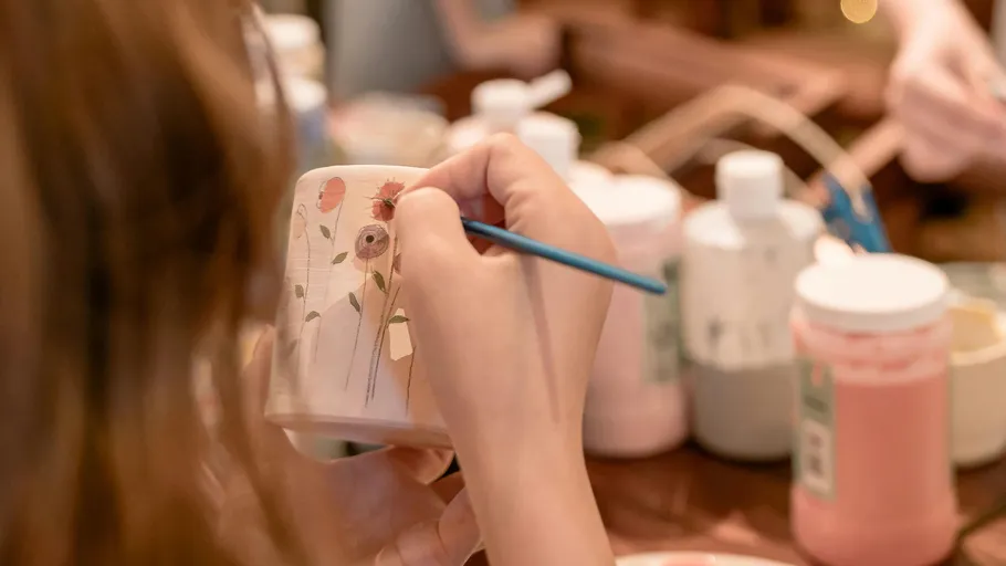 Person decorating mug with paintbrush in studio.