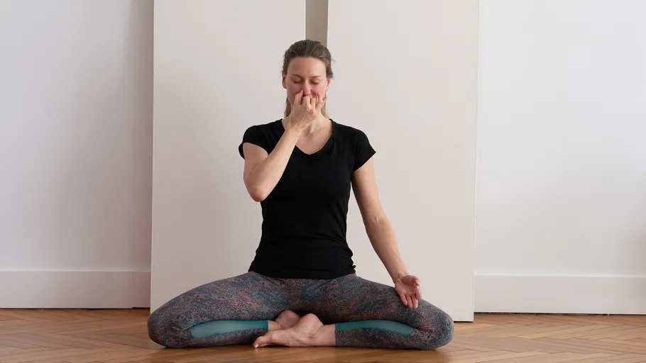 Person übt Yoga-Atemtechnik drinnen aus.
