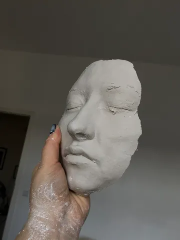 Hand holding a clay face sculpture indoors.