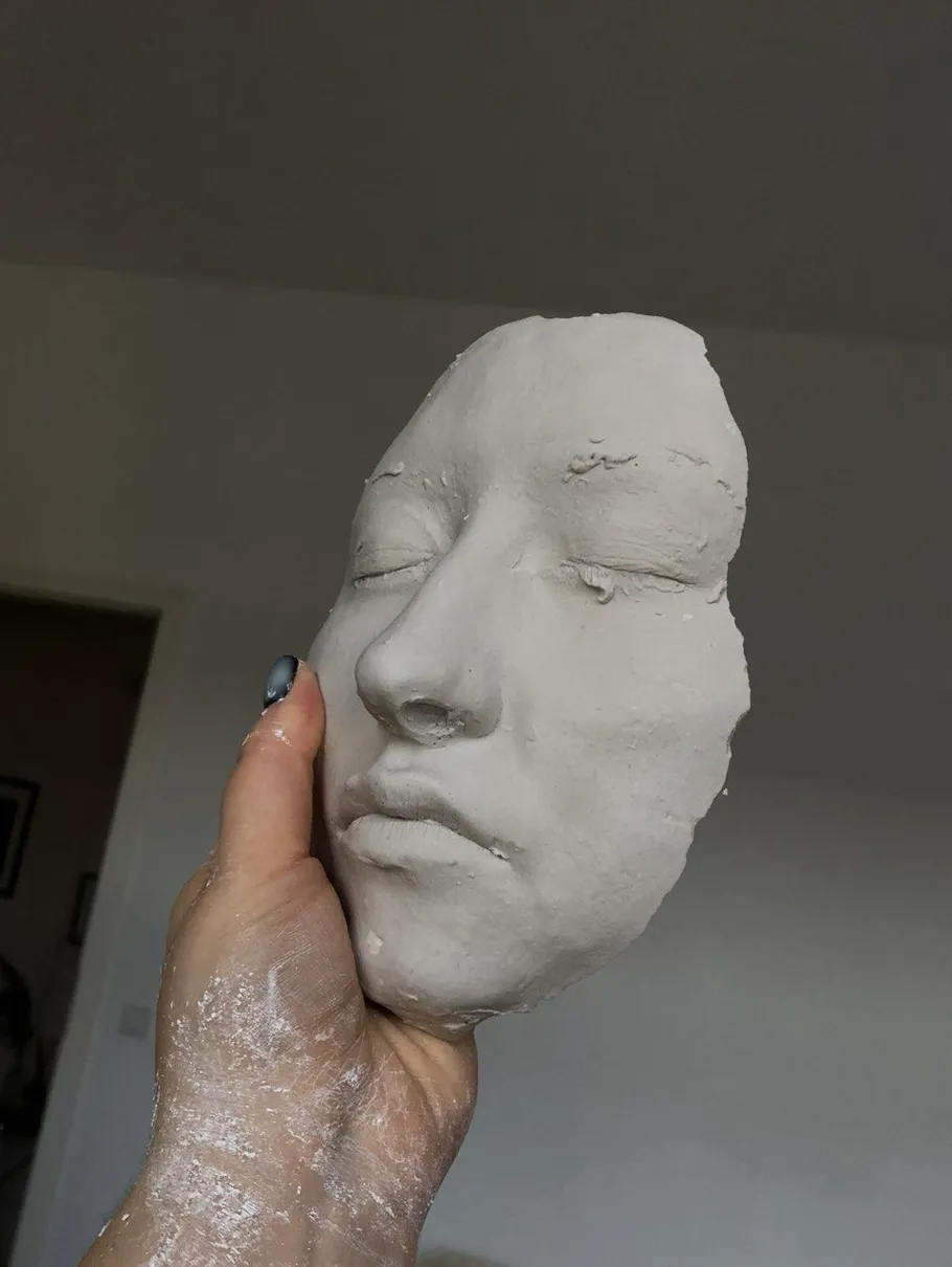 Hand holding a clay face sculpture indoors.