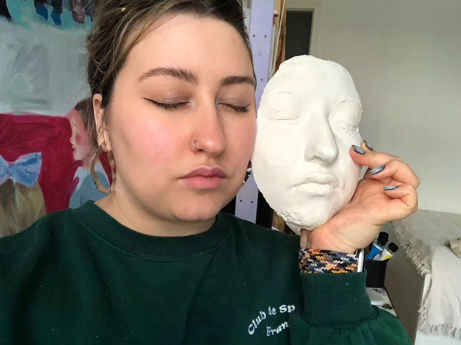 Person hält eine Gesichtsskulptur drinnen.