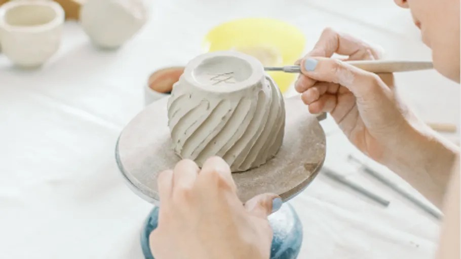 Person schnitzt Tonkrug auf Drehscheibe.