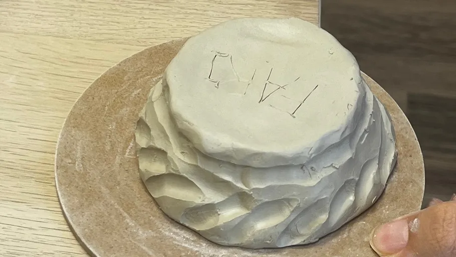 Tonskulptur mit Initialen auf Holztisch.