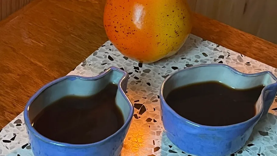 Two blue cups with black coffee beside orange fruit.