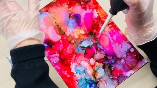 Hands creating vibrant alcohol ink artwork.