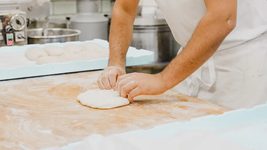 Baker kneading dough on wooden table.