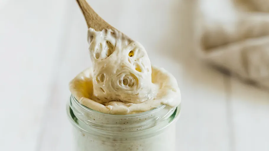 Wooden spoon scooping sourdough starter from jar.