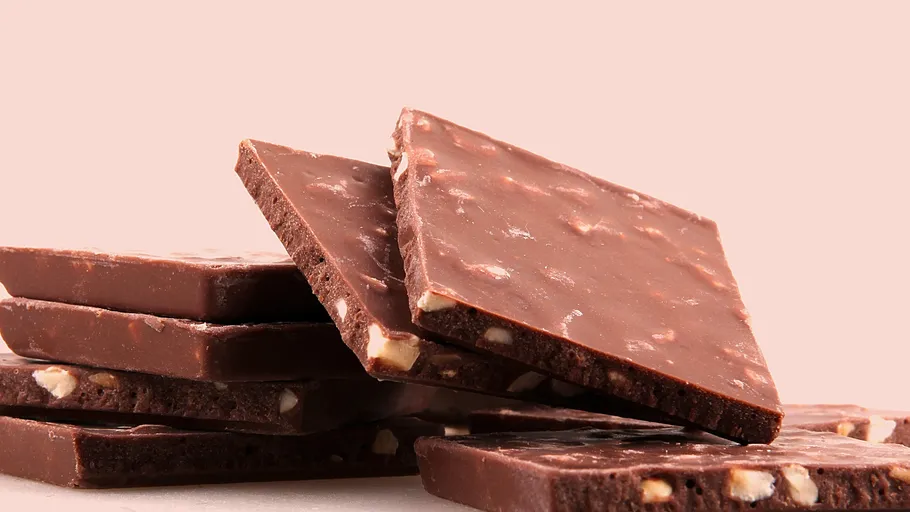 Stacked chocolate bars with nuts on pink background.