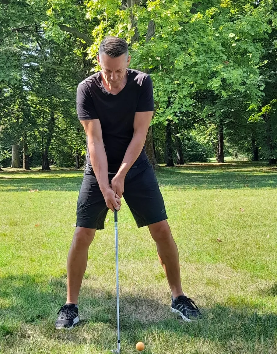 Man preparing to hit golf ball outdoors.