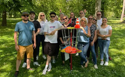 Group posing with disc golf target in park.