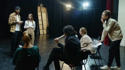Actors rehearsing on stage with a director observing.