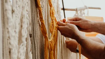 Hands weaving yellow yarn into macramé outdoors.