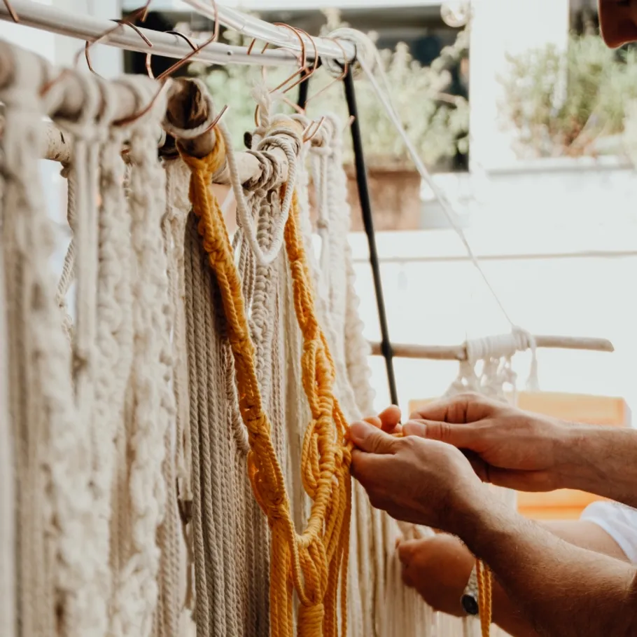 Hands weaving yellow yarn into macramé outdoors.