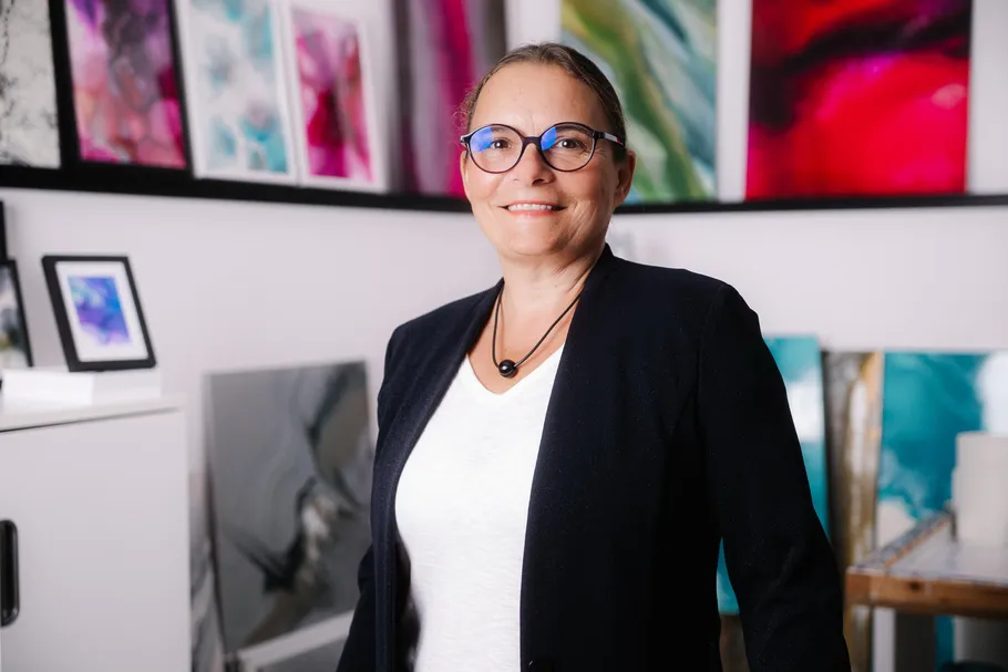 Person smiling, standing in art-filled room.