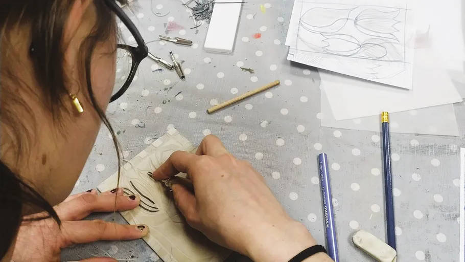 Person carving design on linoleum at table.