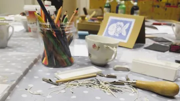 Kunstmaterialien und Teetasse auf Basteltisch.