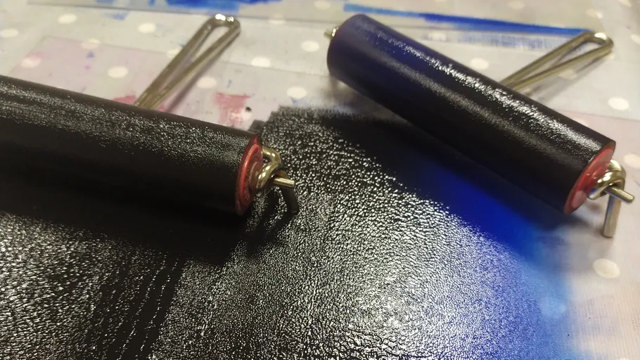 Zwei Farbwalzen verteilen schwarze Tinte auf Oberfläche.
