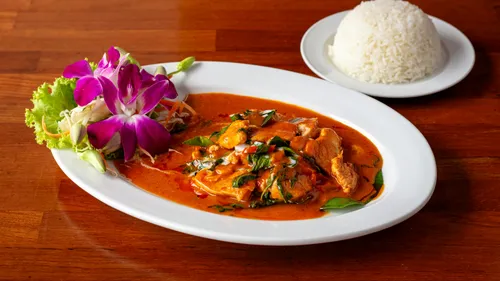 Thai curry with flowers, rice on wooden table.