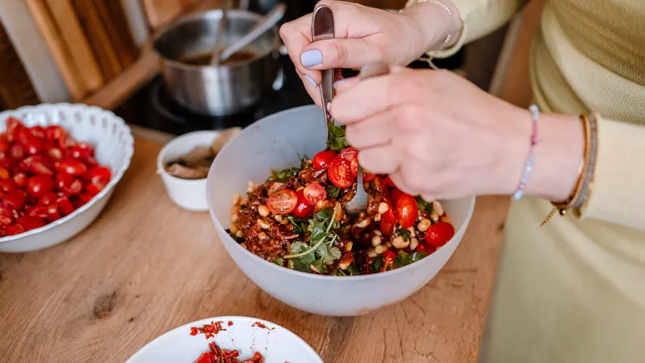 Person preparing salad with tomatoes in a bowl.
