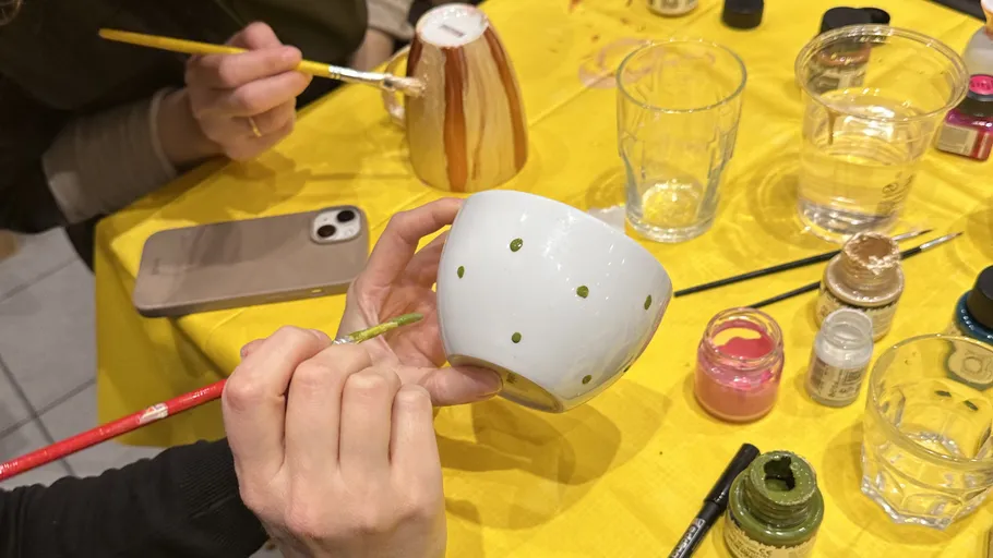 People painting ceramic mugs on a yellow table.