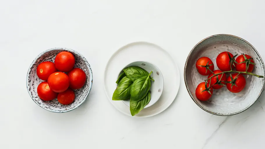 Tomatoes, basil, and cherry tomatoes on plates.