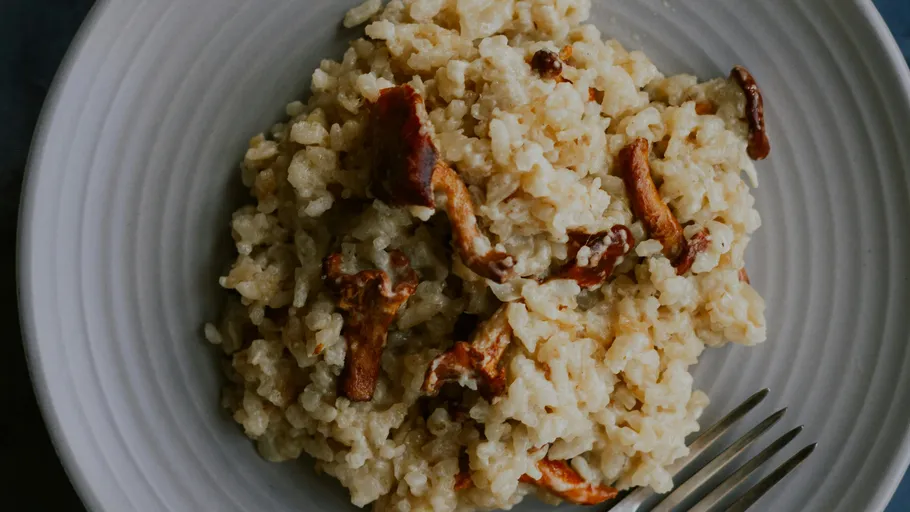Pilzrisotto auf einem weißen Teller mit Gabel.