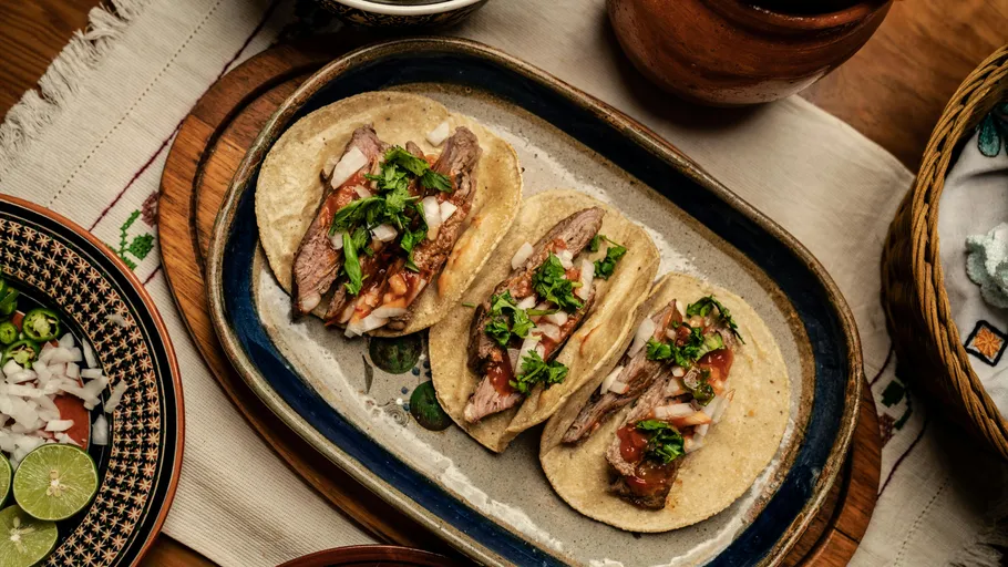 Drei Tacos auf einem Keramikteller, garniert mit Belägen.