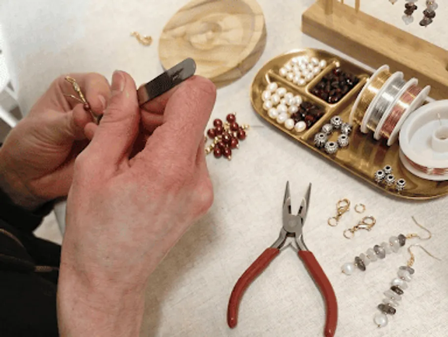 Hands crafting jewelry with beads and tools.