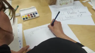 Person übt Kalligraphie an einem Tisch.