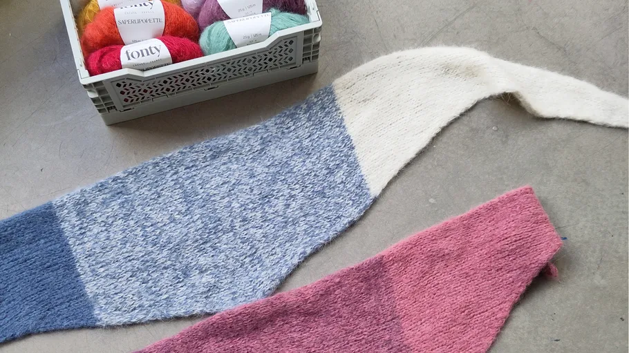 Knitted shawls on floor, yarn in crate.